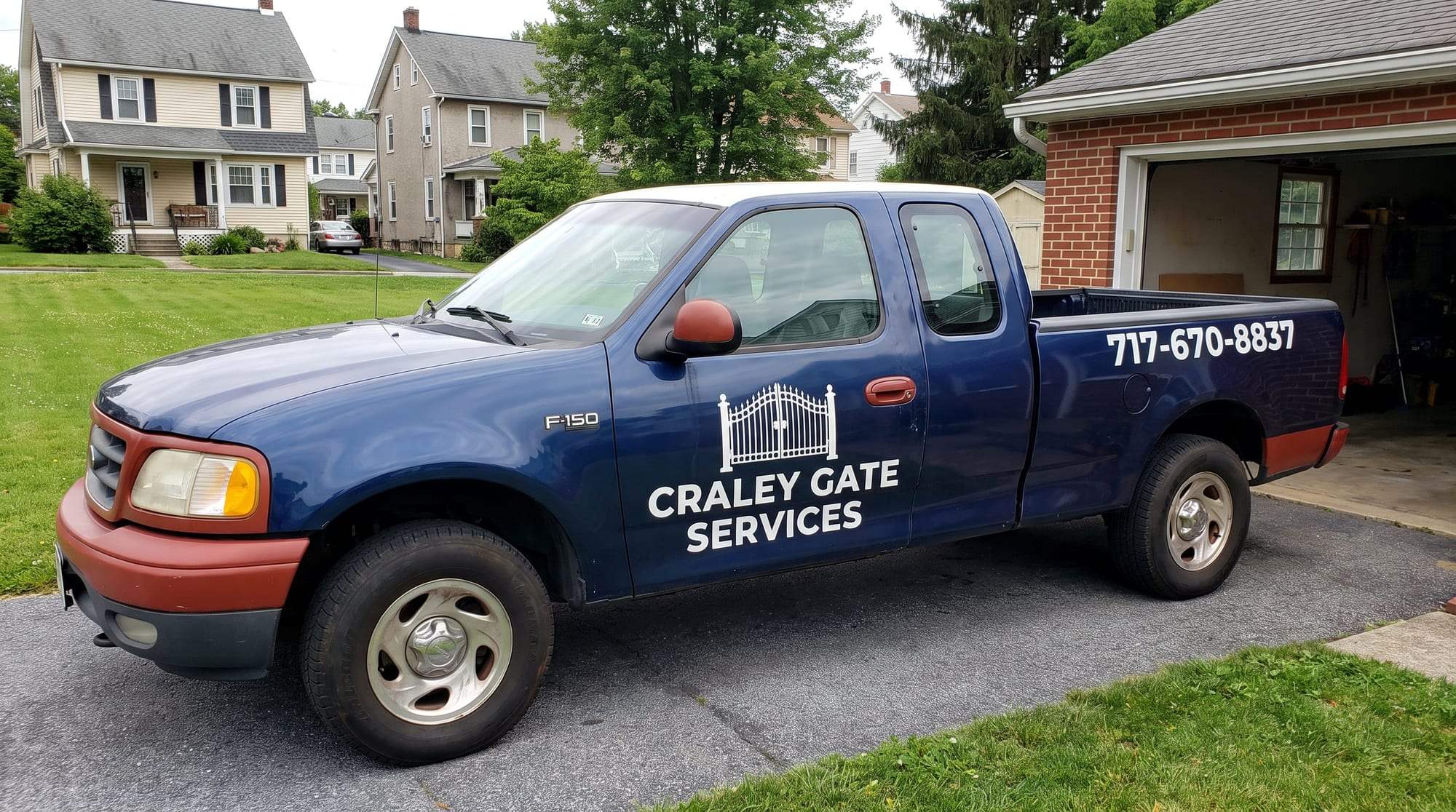 Navy blue Craley Gate Services pickup truck with brick-red trim, the white gate logo and company name on the door and 717-670-8837 on the bed, parked on an asphalt driveway on a residential street